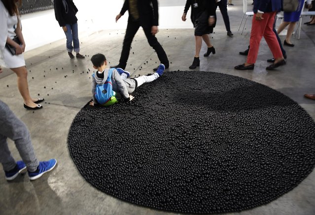 A boy falls as he steps on an artwork “Turbulence (black)” created by Lebanon artist Mona Hatoum during the VIP preview of the art fair “Art Basel” in Hong Kong, Tuesday, March 22, 2016. A set of gold-plated metal cubes, tapestries embroidered by unknown North Korean artisans and bales of cardboard waste are among the highlights of the Art Basel Hong Kong fair opening this week. (Photo by Kin Cheung/AP Photo)