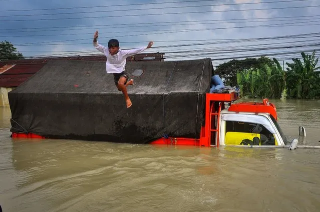 A boy jumps into the floodwaters on the national highway caused by heavy rain and the river bursting in Demak, Central Java on February 11, 2024. (Photo by Akrom Hazami/AFP Photo)