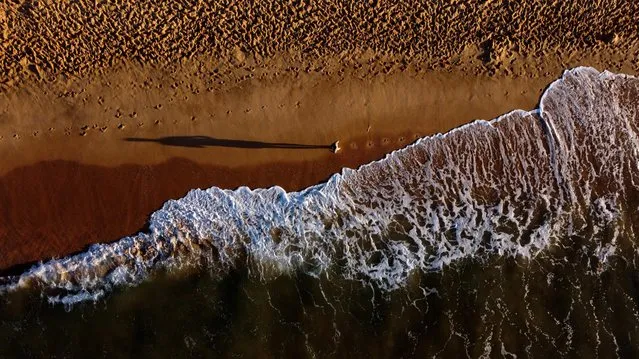 A person runs along the beach in Olhos de Agua, Albufeira, Portugal, October 28, 2021. Picture taken with a drone. (Photo by Carl Recine/Reuters)