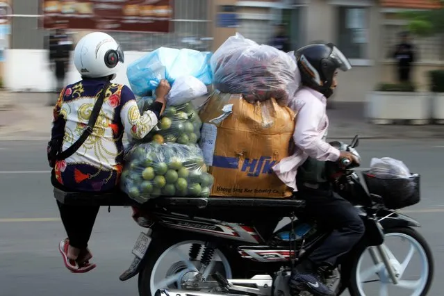 A motorcycle taxi driver carries a vendor on an extended seat on his motorcycle to a market, in Phnom Penh, Cambodia, Wednesday, August 18, 2021. (Photo by Heng Sinith/AP Photo)