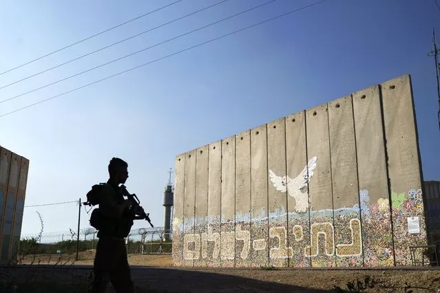 A member of Israeli forces stands next to a security wall written in Hebrew “Path to Peace” at the kibbutz Netiv Haasara near the border with Gaza Strip, Israel, Friday, November 17, 2023. The kibbutz, located close to the Gaza Strip's separation fence with Israel, was attacked during the Hamas cross-border attack on Oct. 7, killing members of its community. (Photo by Leo Correa/AP Photo)