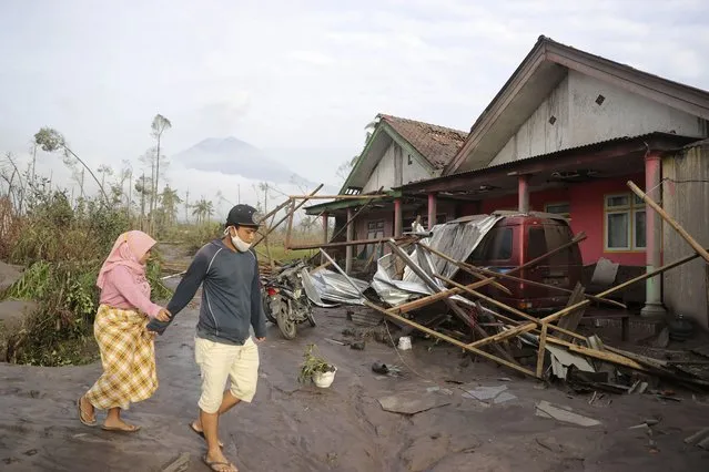 Villagers walk near their damaged home in an area affected by the eruption of Mount Semeru in Lumajang, East Java, Indonesia, Sunday, December 5, 2021. The highest volcano on Indonesia’s most densely populated island of Java spewed thick columns of ash, searing gas and lava down its slopes in a sudden eruption triggered by heavy rains on Saturday. (Photo by Trisnadi/AP Photo)