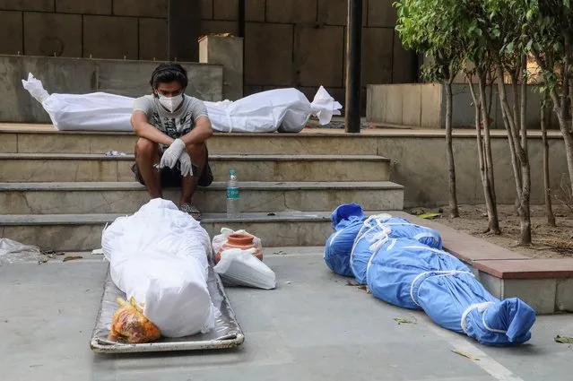 A man wearing a face mask sits next to the bodies of those who have died from the coronavirus Covid-19 virus for cremation at a crematorium in New Delhi, India on April 28, 2021. India faces the world fastest growing number of Covid-19 cases with 360,927 new confirmed infections, the highest single day count in the country and more than 3,293 death in the month of April 2021. (Photo by Naveen Sharma/SOPA Images/Rex Features/Shutterstock)