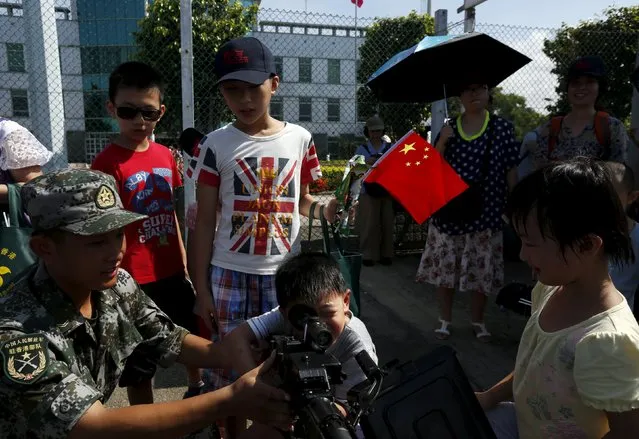A visitor holding a Chinese national flag while wearing a T-shirt featuring a union flag, also known as the Union Jack, looks on as another one tries a weapon at a People's Liberation Army naval base in Hong Kong July 1, 2015. (Photo by Bobby Yip/Reuters)