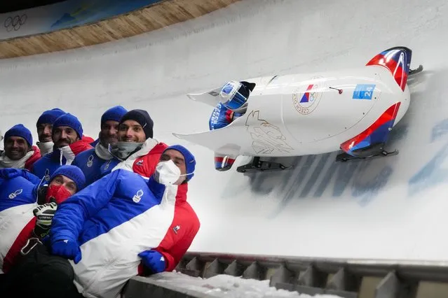 Members of the Czech Republic team pose for a photo as teammates Dominik Dvorak and Jakub Nosek slide past during the 2-man heat 1 at the 2022 Winter Olympics, Monday, February 14, 2022, in the Yanqing district of Beijing. (Photo by Dmitri Lovetsky/AP Photo)