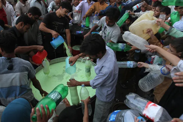 People extend their bottles to get milk mixed with fruit juice to break the day's fast, that many Muslims practice during the month of Ramadan in Karachi, Pakistan, Friday, July 3, 2015. (Photo by Fareed Khan/AP Photo)