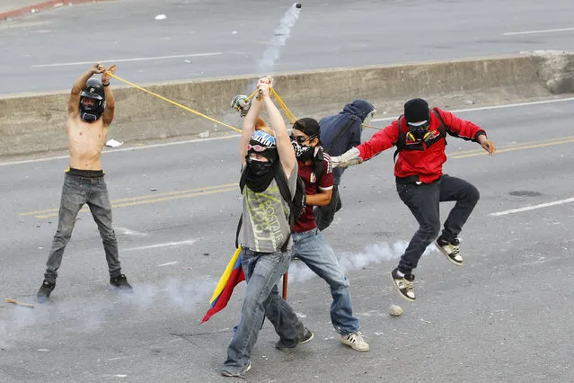 Anti-government protesters use a slingshot to throw rocks at police while jumping to avoid gas canisters during a demonstration in which masked youths battled police and blocked a main highway in Caracas April 21, 2014. Anti-Maduro protests since early February have led to violence killing at least 41 people, according to official figures. The dead have been from both sides of the South American nation's political divide and from security forces. (Photo by Christian Veron/Reuters)