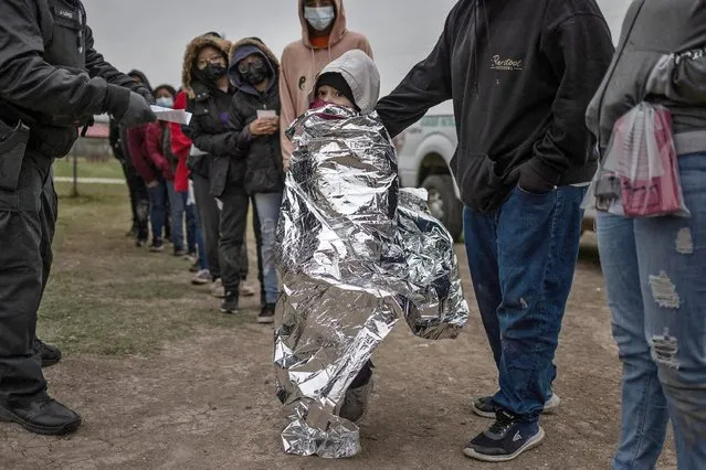 Nelli, a six year old unaccompanied migrant girl from Honduras, stands wrapped in an emergency blanket as she is asked by a Customs and Border Protection official to board a bus after she and others crossed the Rio Grande river into the United States from Mexico, in La Joya, Texas, U.S., February 23, 2022. Nearly a dozen unaccompanied children, who were seeking asylum from El Salvador, Guatemala, Honduras and Nicaragua, were supplied blankets as a cold front dropped temperatures to a blustery 43 Fahrenheit (6.1 Celsius). (Photo by Adrees Latif/Reuters)