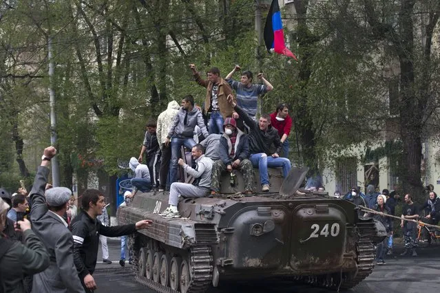 People greet pro-Russian activists atop of a government forces armored personal carrier captured from the enemy in fighting  in Mariupol, eastern Ukraine, Friday, May 9, 2014. Fighting exploded Friday in Mariupol, a city of 500,000 on the Sea of Azov that is on the main road between Russia proper and Crimea. The fighting between government forces and insurgents in Mariupol has left several people dead. (Photo by Alexander Zemlianichenko/AP Photo)