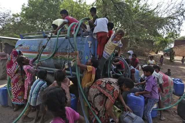 Indian women and children struggle to collect government-supplied water from a mobile tanker in Ramol, outskirts of Ahmadabad, India, Sunday, May 11, 2014. As India faces certain water scarcity and ecological decline, the country's main political parties campaigning for elections have all but ignored environmental issues seen as crucial to India's vast rural majority, policy analysts say. (Photo by Ajit Solanki/AP Photo)