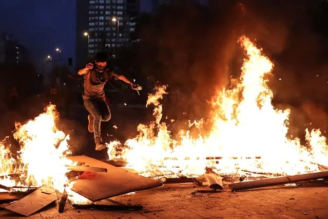 A demonstrator jumps over a burning barricade during a protest against Chile's government in Santiago, Chile on November 12, 2019. (Photo by Ivan Alvarado/Reuters)