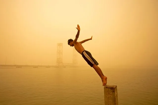 A youth dives in the Shatt al-Arab river during a sandstorm in Iraq's southern city of Basra on May 16, 2022. Another sandstorm that descended on climate-stressed Iraq sent at least 4,000 people to hospital with breathing problems and led to the closure of airports, schools and public offices across the country. (Photo by Hussein Faleh/AFP Photo)