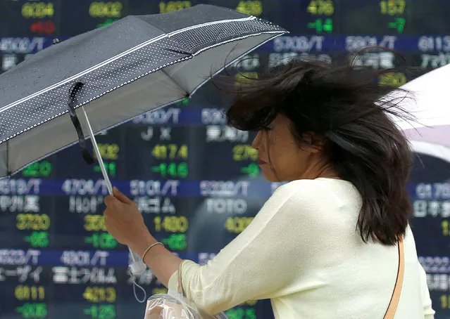 A pedestrian holding an umbrella struggles against strong wind and rain as she walks past a stock quotation board outside a brokerage in Tokyo, Japan, June 13, 2016. (Photo by Issei Kato/Reuters)