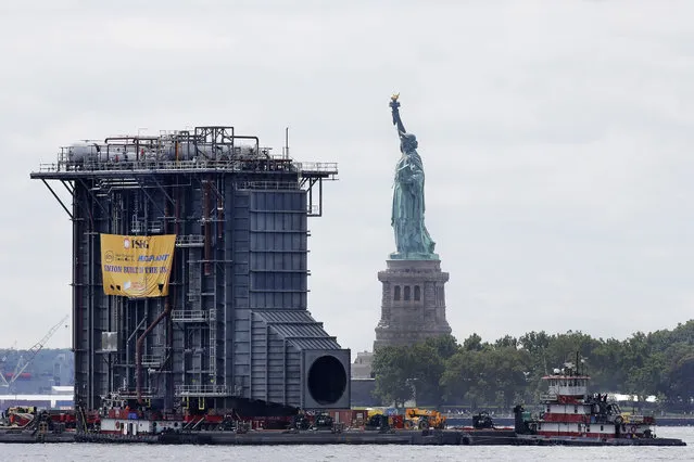 Tugboats guide a barge laden with a $195 million heat-recovery steam generator past the Statue of Liberty, Tuesday, August 8, 2017, in New York. The generator is a component of a new, $600 million power plant being built by PSEG. The equipment was assembled in Coeymans, N.Y. and is destined for the Sewaren 7 power plant in Woodbridge, N.J. (Photo by Mark Lennihan/AP Photo)