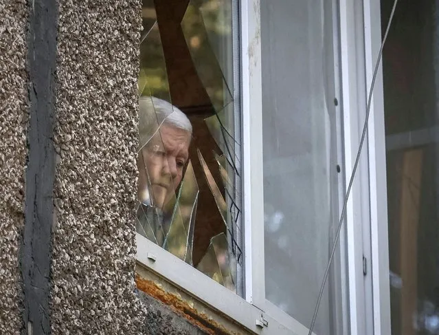 A local resident looks out through a broken window at a school building damaged by a Russian military strike, amid Russia's invasion on Ukraine, in the town of Kostiantynivka, Ukraine on July 13, 2022. (Photo by Gleb Garanich/Reuters)
