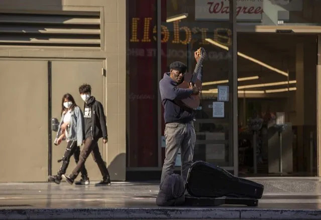 A lone street performer tunes his guitar on a mostly-empty Hollywood Boulevard in Los Angeles, Tuesday, March 24, 2020. New cases of the coronavirus surged around the state. (Photo by Damian Dovarganes/AP Photo)