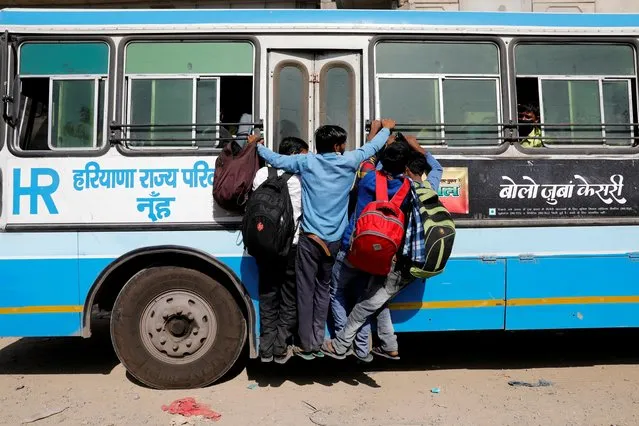 Migrant workers hang on to a door of their moving bus as they return to their villages in Ghaziabad, on the outskirts of New Delhi, March 29, 2020. (Photo by Adnan Abidi/Reuters)