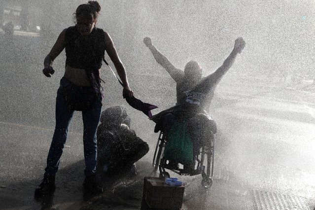 A riot police vehicle releases water on demonstrators during a rally on the fourth anniversary of the protests and riots that rocked the country in 2019, in Santiago, Chile on October 18, 2023. (Photo by Ivan Alvarado/Reuters)