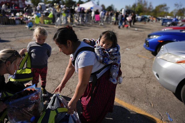 Silvia, only first name given, picks up donated items while carrying her child at an aid center for people affected by wildfires at Santa Anita Park Monday, January 13, 2025, in Arcadia, Calif. (Photo by Carolyn Kaster/AP Photo)