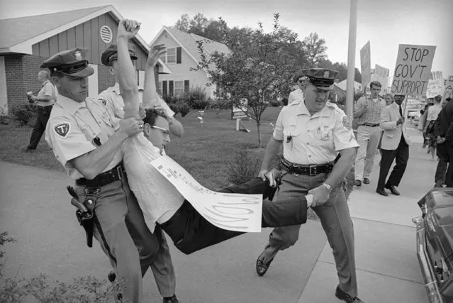 Prince Georges County police carry an integrationist  to a waiting patrol car in Bowie, Maryland on September 7, 1963 after he and 11 other persons were arrested and charged with trespassing at the sales office of a housing development here. The 12 lay down on the floor of the office of Levitt & Sons, developer of Bolair, and refused to move. They were protesting the firm's refusal to sell homes to African Americans. (Photo by AP Photo/WAS)