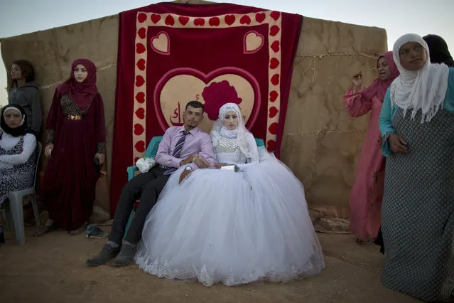 In this Friday, August 7, 2015 file photo, Syrian refugee groom Ahmad Khalid, 21, and his bride Fatheya Mohammed, 21, sit in front of his family's tent during their wedding ceremony at an informal tented settlement near the Syrian border on the outskirts of Mafraq, Jordan. (Photo by Muhammed Muheisen/AP Photo)