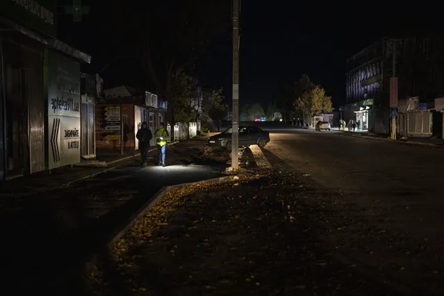 People walk along a street during a power outage, in Borodyanka, Kyiv region, Ukraine, Thursday, October 20, 2022. Airstrikes cut power and water supplies to hundreds of thousands of Ukrainians on Tuesday, part of what the country's president called an expanding Russian campaign to drive the nation into the cold and dark and make peace talks impossible. (Photo by Emilio Morenatti/AP Photo)
