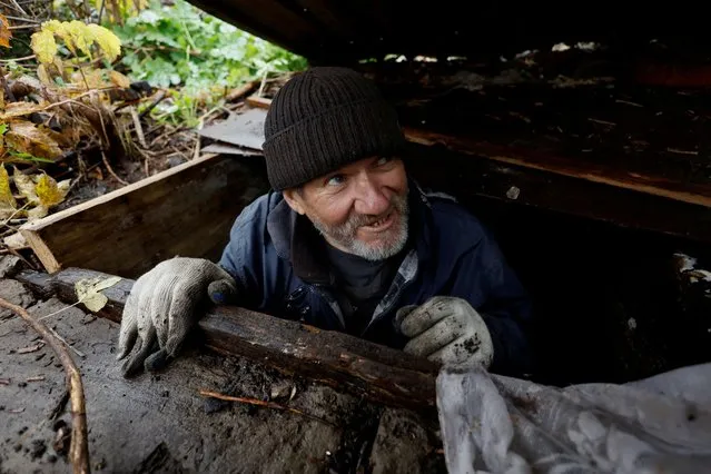 Myhaylo Yurkiv, 65, climbs out of the small bunker he stayed in for six months during fierce battles under Russian occupation which destroyed every home in the village and cut the village in two by the shelling of the bridge, leaving him now as the only person living on his side of the village, as Russia's invasion of Ukraine continues, in Tsupivka, Ukraine on October 26, 2022. (Photo by Clodagh Kilcoyne/Reuters)