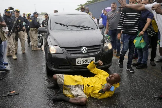 A supporter of President-elect Luiz Inacio Lula da Silva slips on a rain soaked pavement as he continues to chant slogans surrounded by truckers loyal to outgoing President Jair Bolsonaro blocking a highway, in Itaborai, Rio de Janerio state, Brazil, Tuesday, November 1, 2022. Truckers supportive of Bolsonaro blocked hundreds of roads early Tuesday to protest his election loss to Lula da Silva. (Photo by Silvia Izquierdo/AP Photo)