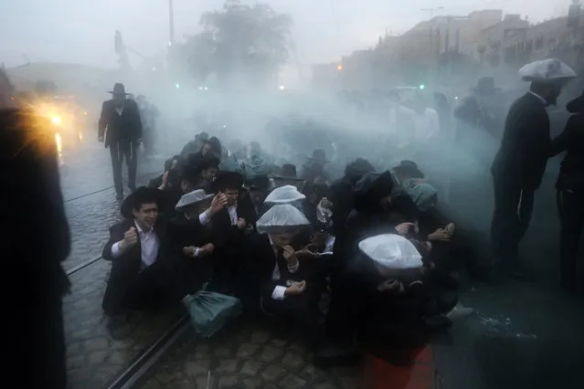 Members of the Israeli security forces spray water as they try to disperse ultra-Orthodox Jews from blocking the road in a demonstration against Israeli army conscription in Jerusalem on November 26, 2017. Many ultra-Orthodox oppose military service for their young men because they believe it exposes them to influences and temptations not found in the insular world of prayer and religious study. (Photo by Menahem Kahana/AFP Photo)