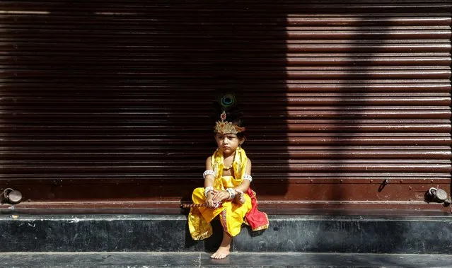 An Indian child dressed as Lord Krishna sits infront of a closed shop on the occasion of the Janmashtami Festival in Mumbai, India, 25 August 2016. According to reports, the Supreme Court banned minors to participate in forming human pyramids and ordered to limit the height of human pyramids to 20 feet. The festival celebrates the birth of the Hindu god Lord Krishna, one of the most popular gods in Hinduism. (Photo by Divyakant Solanki/EPA)