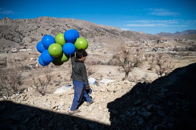 An Afghan boy holds balloons as he walks downhill along a path in Barmal district of Paktika province on December 15, 2022. (Photo by Wakil Kohsar/AFP Photo)