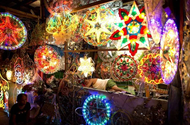 A vendor (C) sleeps amongst christmas lanterns known locally as “parol” on display along a street in Manila on November 18, 2014. Parol are star-shaped Christmas lanterns patterned to resemble the Star of Bethlehem, and are made from bamboo covered with paper. They are displayed in houses, offices, buildings, and streets, and according to Filipino tradition and beliefs, also represent the victory of light over darkness. (Photo by Noel Celis/AFP Photo)