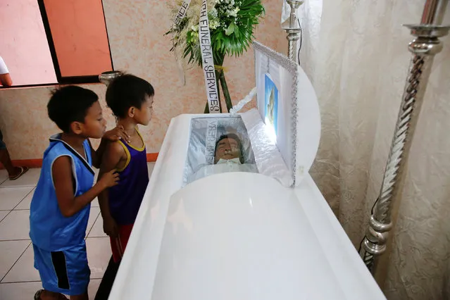 Children look inside a coffin with a man whose body was found earlier this week with a placard accusing him of being a drug pusher, in a community centre where relatives and friends gathered to mourn his death in Manila, Philippines October 8, 2016. (Photo by Damir Sagolj/Reuters)