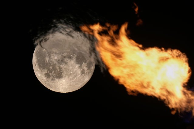 The full moon is seen behind the flame of a gas torch on top of a Rostral column in St. Petersburg, Russia, Saturday, August 9, 2025. (Photo by Dmitri Lovetsky/AP Photo)
