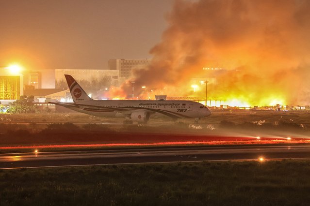 An airline plane stands on the tarmac as firefighters try to extinguish a fire that broke out in the cargo section of Hazrat Shahjalal International Airport in Dhaka on October 18, 2025. (Photo by Maruf Rahman/AFP Photo)