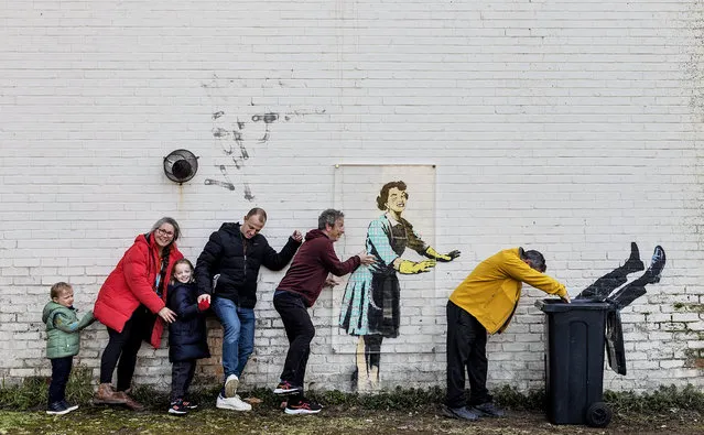 A family do the conga next to a new artwork called “Valentine’s Day mascara” on February 15, 2023 in Margate, England. The image, which centres on the theme of violence against women and girls, appeared yesterday, alongside a refrigerator, which featured as part of the artwork. The fridge was promptly moved by Thanet district council, who said it would return “once it has been made safe”. Since then a wheelie bin has appeared as a replacement and a sheet of plastic covering the image with a sign reading 'do not touch'. The artwork now appears to have two private security guards despite being on the wall of a privately owned house backing onto council run property. Locals anticipate the piece will likely be removed and sold at auction. (Photo by Dan Kitwood/Getty Images)