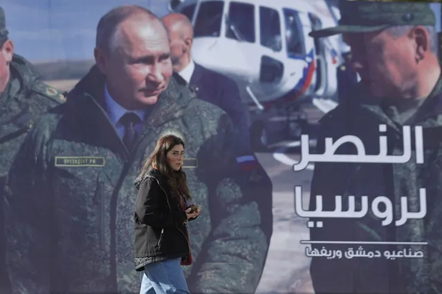 A woman passes a billboard showing Russian President Vladimir Putin in Damascus, Syria, Monday, March 7, 2022. The Arabic in poster reads, “The victory for Russia”. (Photo by Omar Sanadiki/AP Photo)