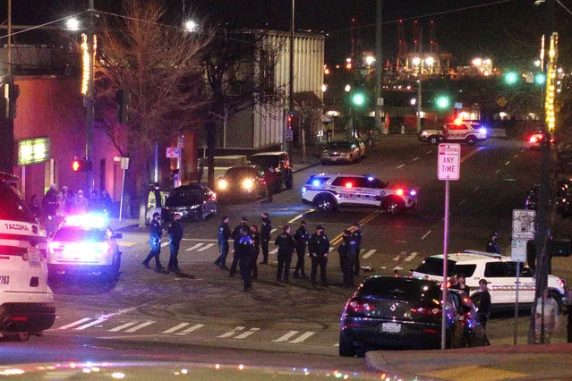 Tacoma Police and other law enforcement officers stand in an intersection near the site of a car crash Saturday, January 23, 2021, in downtown Tacoma, Wash. At least one person was injured when a police car plowed through a crowd of people Saturday night who were watching a downtown street race, the Tacoma News-Tribune reported. (Photo by Ted S. Warren/AP Photo)