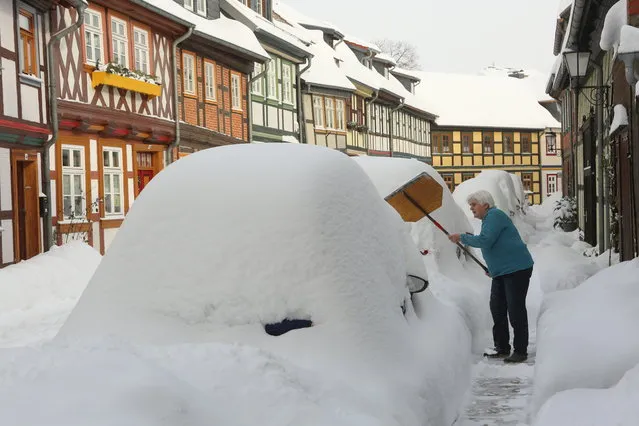 A resident clears the sidewalk in front of her front door of snow in Wernigerode, Germany, Tuesday, February 9, 2021. (Photo by Matthias Bein/dpa via AP Photo)