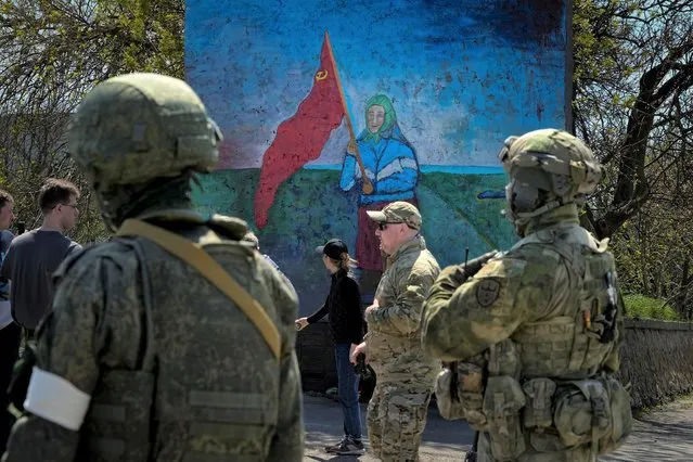 Russian servicemen stand near a painting of a Ukrainian woman holding a Soviet-era red flag in territory under the government of the Donetsk People's Republic, eastern Ukraine, April 30, 2022. Some in the West think Russian President Vladimir Putin may use the Victory Day on May 9 when Russia celebrates the defeat of Nazi Germany in World War II to officially declare that war is underway in Ukraine and announce a mobilization – the claim rejected by the Kremlin. (Photo by Alexander Zemlianichenko/AP Photo)