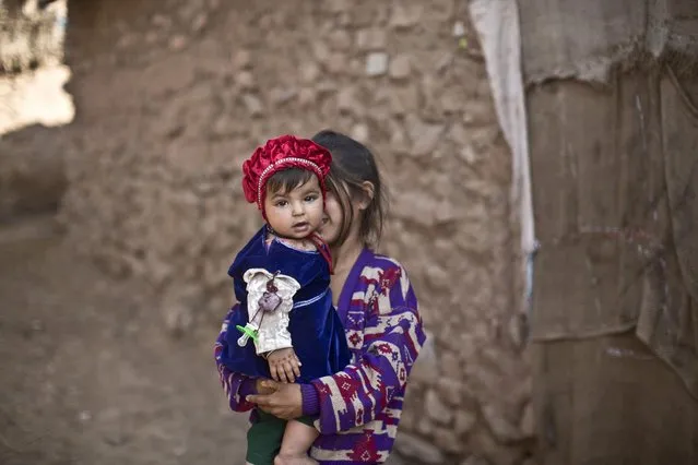 An Afghan refugee girl holds her younger sister in a slum on the outskirts of Islamabad, Pakistan, Sunday, January 18, 2015. (Photo by Muhammed Muheisen/AP Photo)