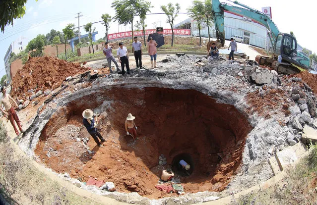 A rescue team works under a caved-in area on a road in Loudi, Hunan province, June 18, 2013. The road surface sank after a truck drove past. A motorcyclist riding behind the truck was injured, according to local reports. (Photo by Reuters/China Daily)