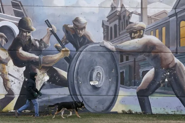 A man walks his dog past a mural depicting factory workers in the historic Pullman neighborhood in Chicago November 20, 2014. U.S. President Barack Obama is expected to announce the designation of the Pullman neighborhood as a national park on February 19, according to park advocates. (Photo by Andrew Nelles/Reuters)