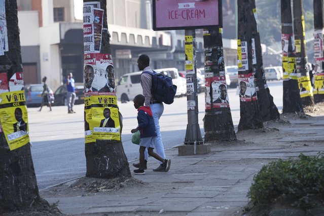 A man and a child walk past trees plastered with campaign posters on the streets of Harare, Sunday, August 20 2023. The upcoming general election in Zimbabwe is crucial to determining the future of a southern African nation endowed with vast mineral resources and rich agricultural land. But for many in the educated but underemployed population, the daily grind to put food on the table inhibits interest in politics. (Photo by Tsvangirayi Mukwazhi/AP Photo)