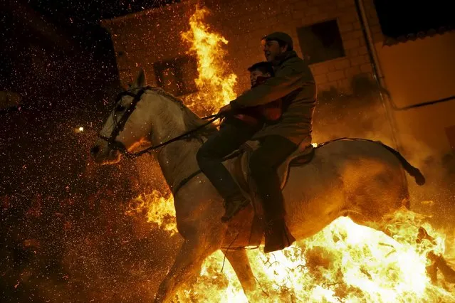 A man rides a horse with a child through the flames during the “Luminarias” annual religious celebration on the eve of Saint Anthony's day, Spain's patron saint of animals, in the village of San Bartolome de Pinares, northwest of Madrid, Spain, January 16, 2016. According to tradition that dates back 500 years, people ride their horses through the narrow cobblestone streets of this small village to purify the animals with the smoke of the bonfires. (Photo by Susana Vera/Reuters)