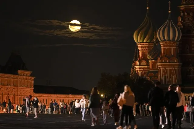 The August Super Blue Moon sets behind a historical building and the St. Basil's Cathedral, right, as people walk in Red Square in Moscow, Russia, Wednesday, August 30, 2023. The cosmic curtain rises Wednesday night with the second full moon of the month, the reason it is considered blue. It is dubbed a supermoon because it is closer to Earth than usual, appearing especially big and bright. (Photo by Alexander Zemlianichenko/AP Photo)