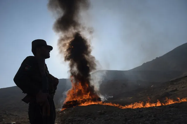 An Afghan policeman watches as a cache of alcohol and drugs burns on the outskirts of Kabul on December 20, 2016. Ninety eight tons of opium, heroin, hashish and alcoholic drinks were set on fire, officials said. (Photo by Shah Marai/AFP Photo)
