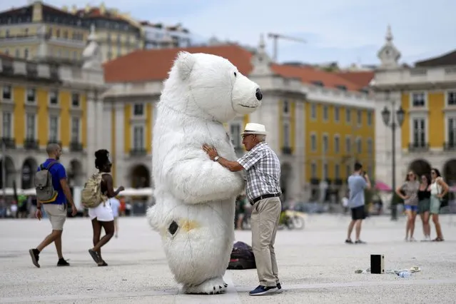 A man talks to a person wearing a polar bear costume at Lisbon's Comercio square, Monday, July 11, 2022. Temperatures in Portugal have dropped in the last couple days bringing some respite from a heatwave but are expected to rise again Tuesday and reach 46 degrees Celsius (115 Fahrenheit) in some parts of the country by Thursday. (Photo by Armando Franca/AP Photo)