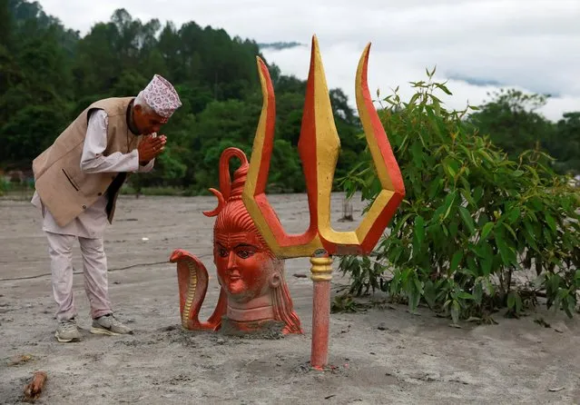 Narayan Prasad Dulal offers prayers on the statue of Lord Shiva submerged in mud after the area was hit by flash floods along the bank of Melamchi River in Sindhupalchok, Nepal on June 20, 2021. (Photo by Navesh Chitrakar/Reuters)