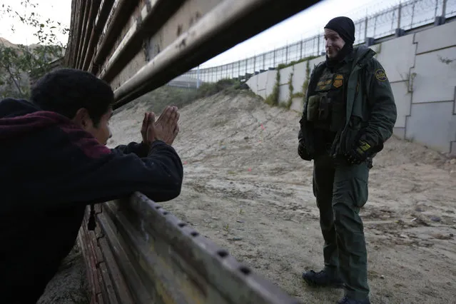 A Honduran migrant pleads with a U.S. Border Patrol agent to let him cross into the U.S., as he peeks through a barrier in Tijuana, Mexico, on Saturday, December 15, 2018. The officer did not respond, and the Honduran did not know the agent would not prevent him from crossing. The man returned to the group of people he was with. (Photo by Moises Castillo/AP Photo)